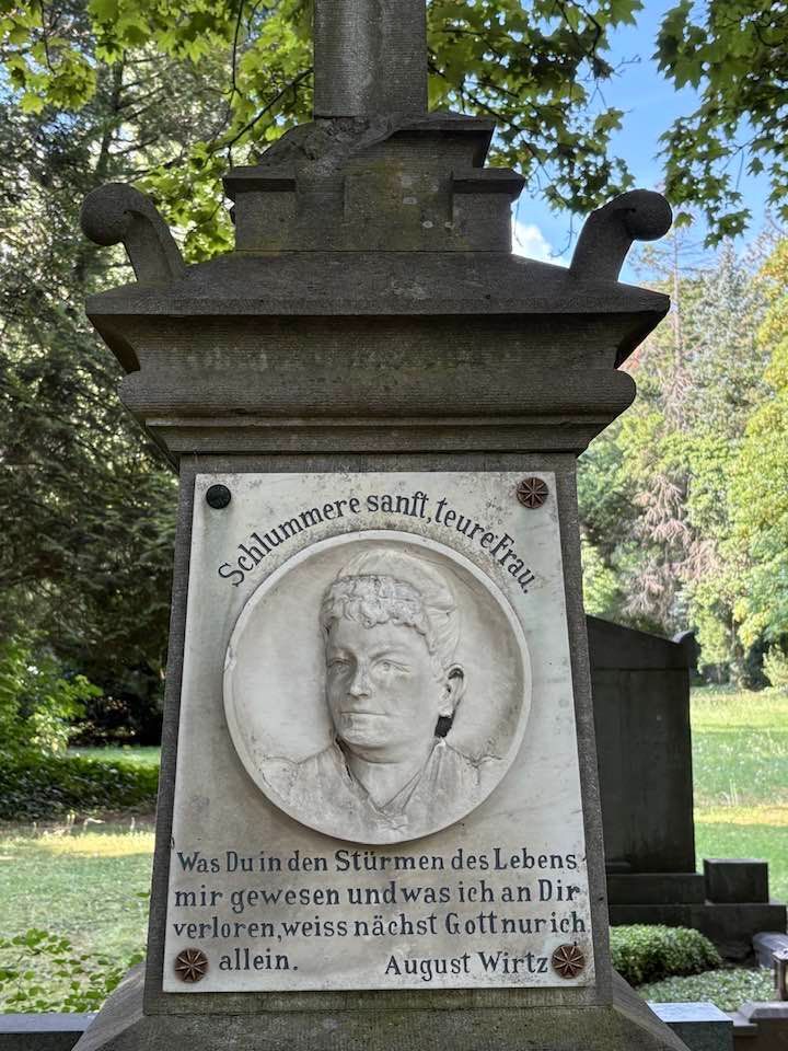 Grabstein mit einem eingemeißelten Frauenporträt; darunter deutsche Inschrift.