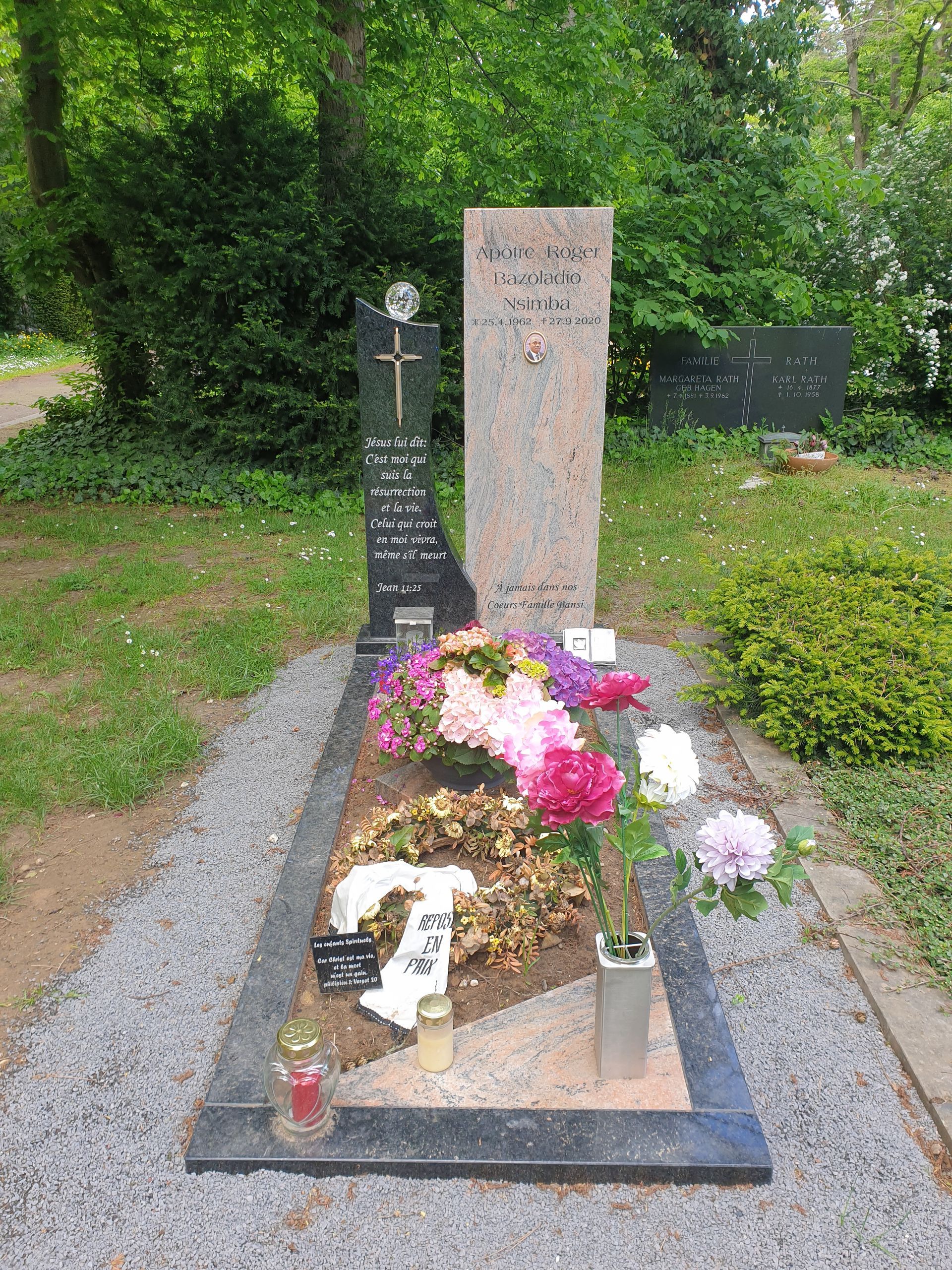 Grab mit zwei Grabsteinen, Blumen und Kerzen; in einem Kiesbeet.