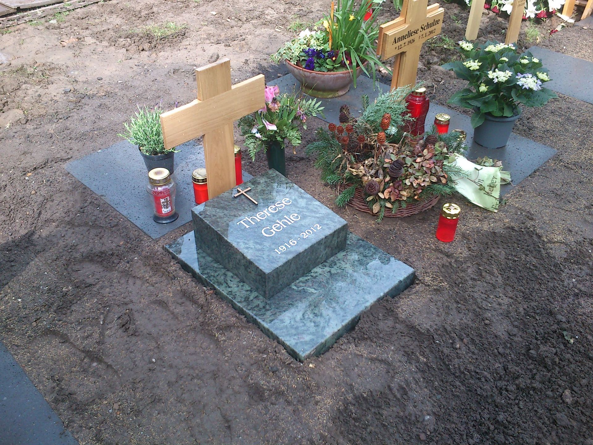 Grab mit Grabstein und Kreuz, Blumen und Kerzen; auf einem Erdbett.