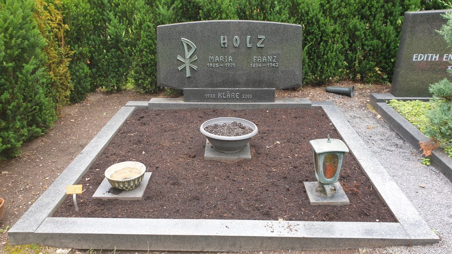 Grab mit einem Grabstein mit Symbol, Pflanzgefäß und zwei dekorativen Halterungen.