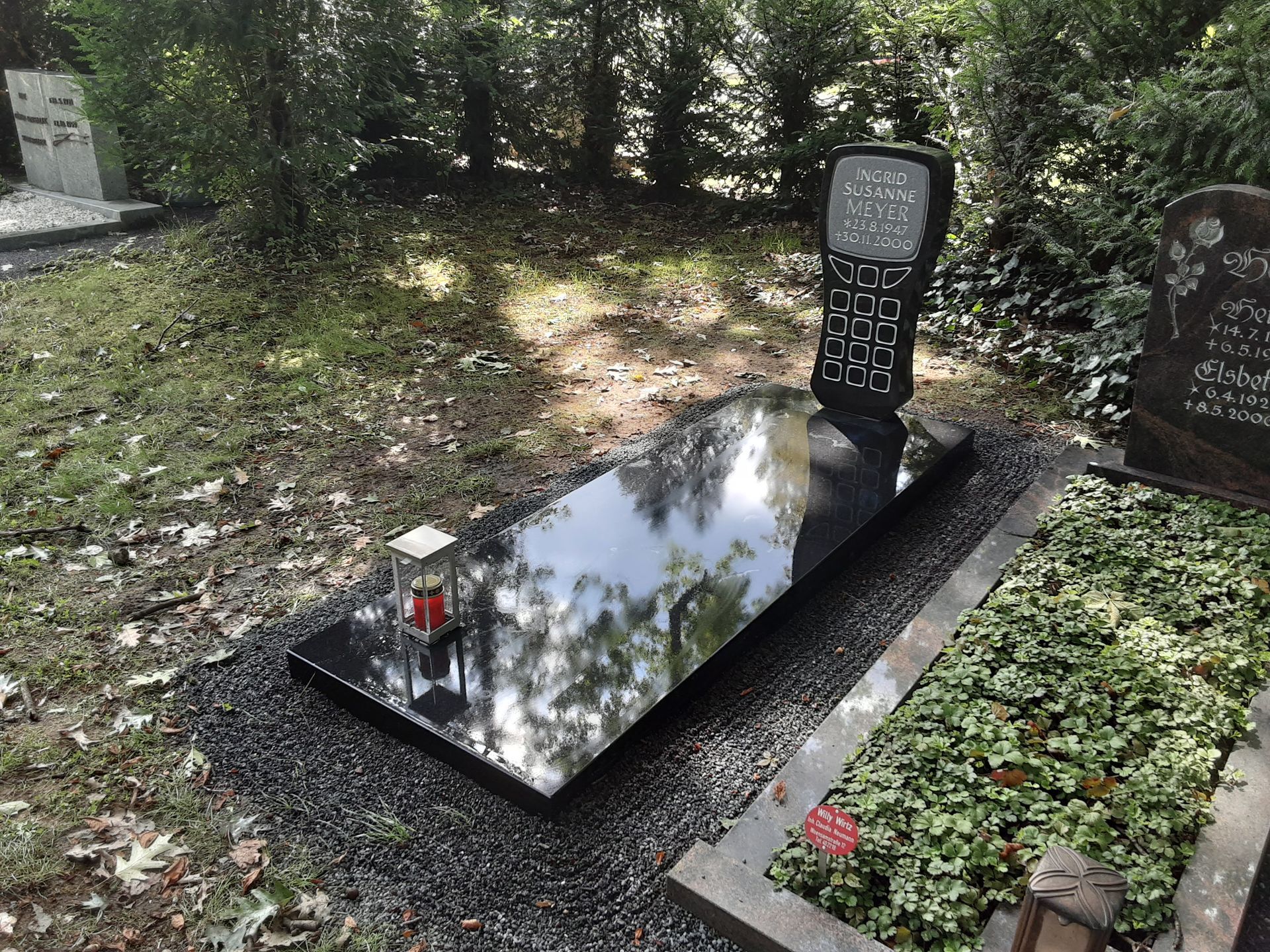 Schwarzer Granitgrabstein mit dekorativem Muster und reflektierender Oberfläche auf einem Friedhof.