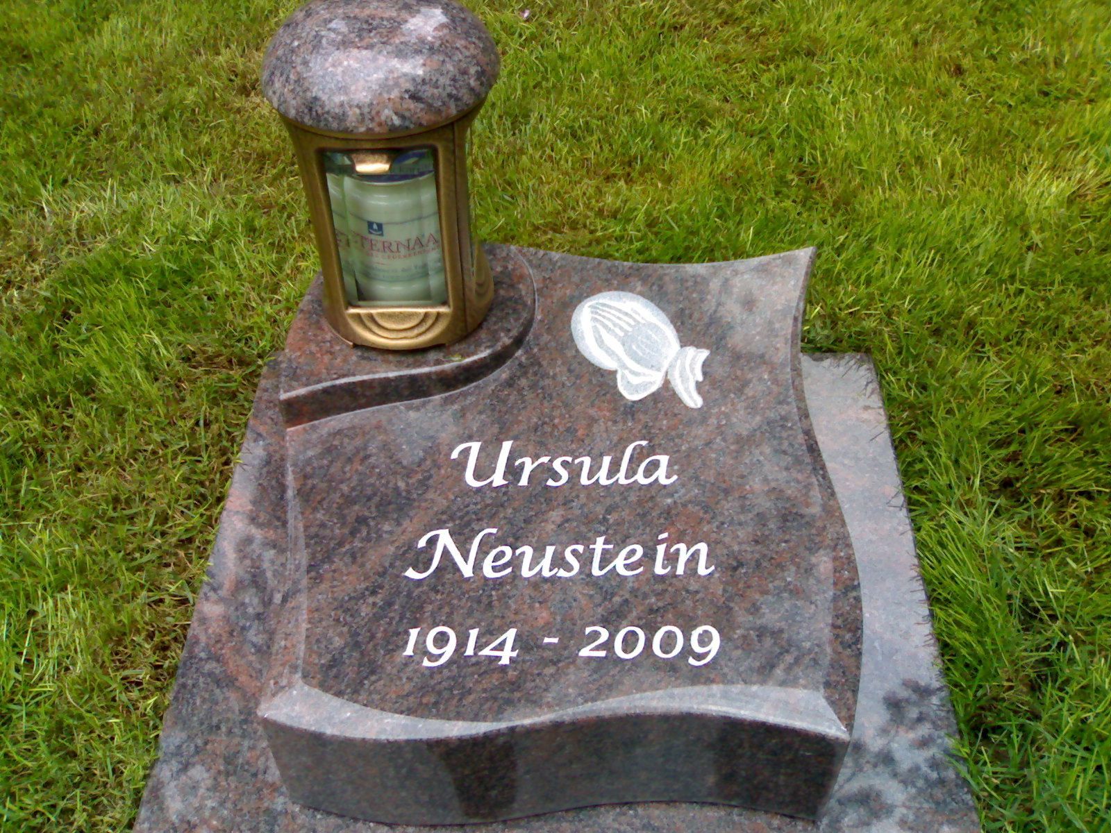 Grabstein von Ursula Neustein mit den Jahreszahlen 1914-2009. Auf dem dunklen Granit steht eine brennende Kerze.