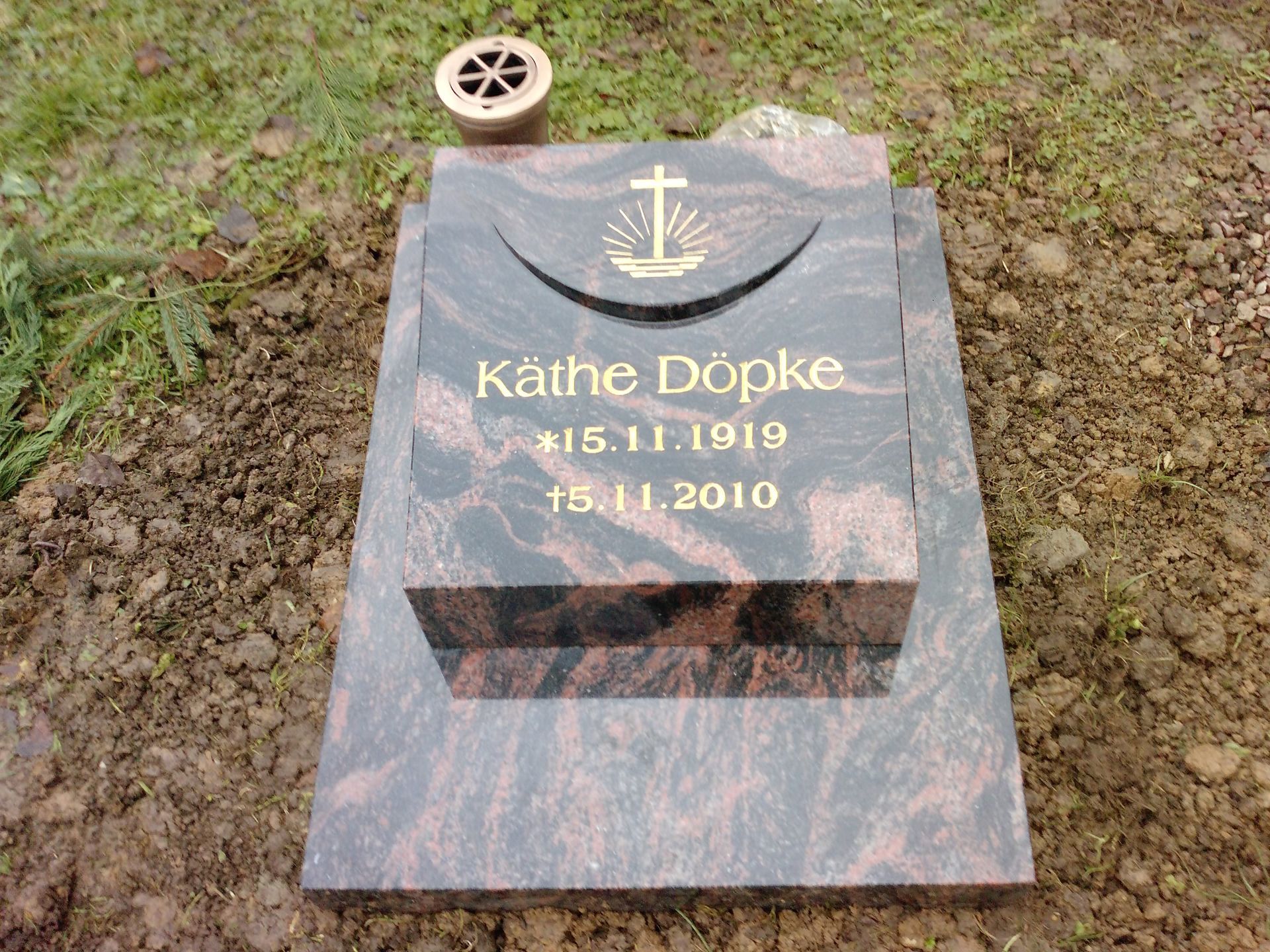 Grabstein von Käthe Döpke, geboren 1919, gestorben 2010. Verziert mit einem Kreuzemblem und befindet sich auf einem Friedhof.