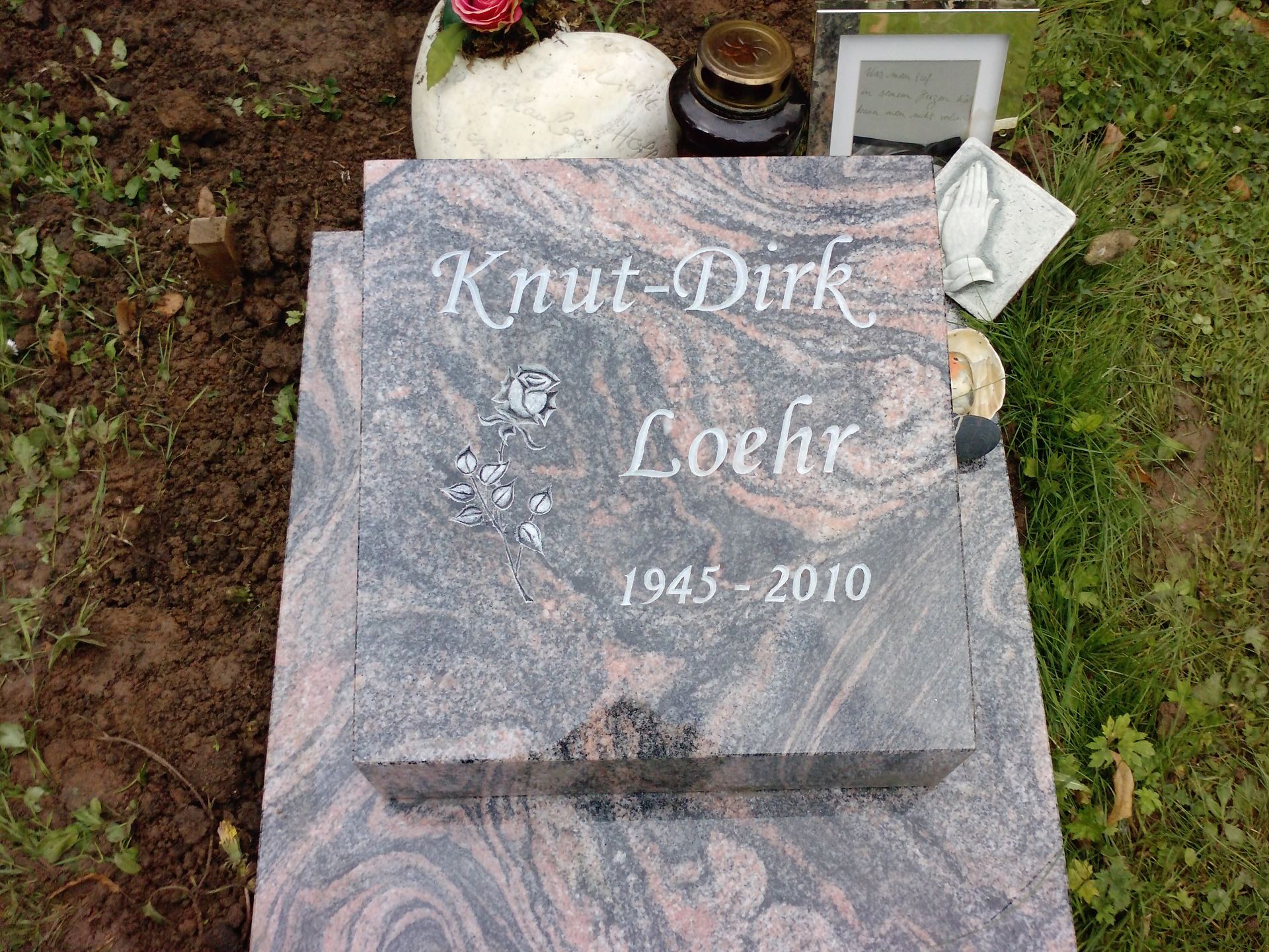 Grabstein für Knut-Dirk Loehr, geboren 1945, gestorben 2010. Grauer und roter Granitstein mit Blumen auf einem grasbewachsenen Grabfeld.