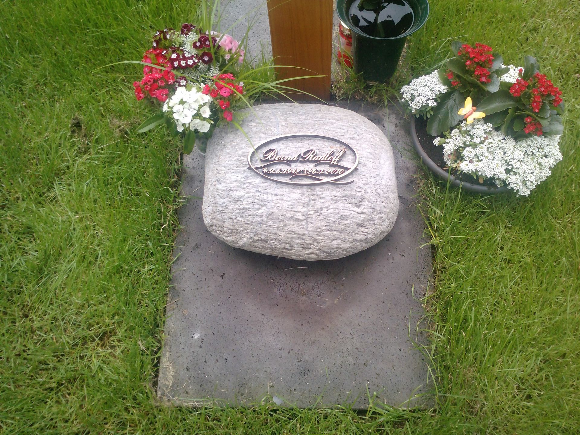 Grab mit Steinmarkierung, Blumen und dunkler Grabplatte.