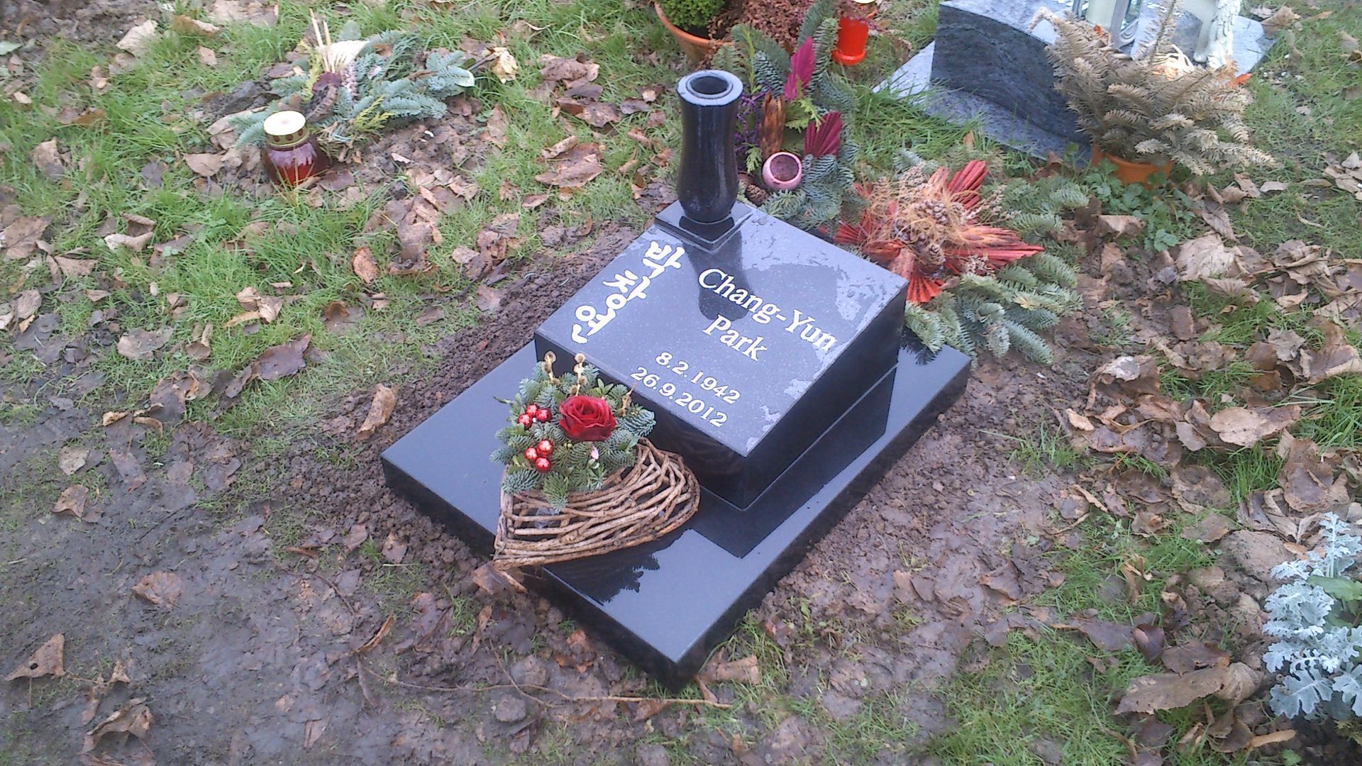 Schwarzer Granitgrabstein mit Blumenarrangement auf einem Friedhof.