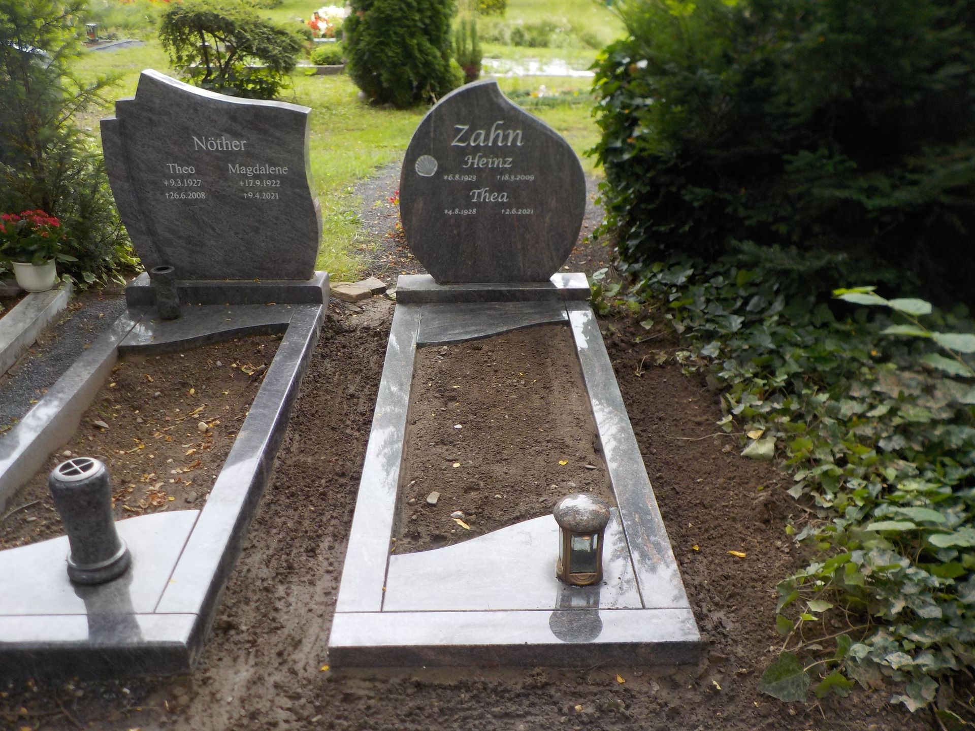 Zwei Granitgrabsteine ​​auf einem Friedhof mit leeren Gräbern davor.