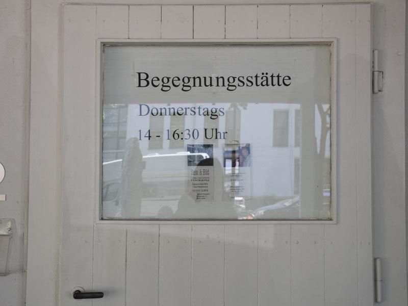 Eine weiße Tür mit einem Schild darauf, auf dem steht: Begegnungsstätte
