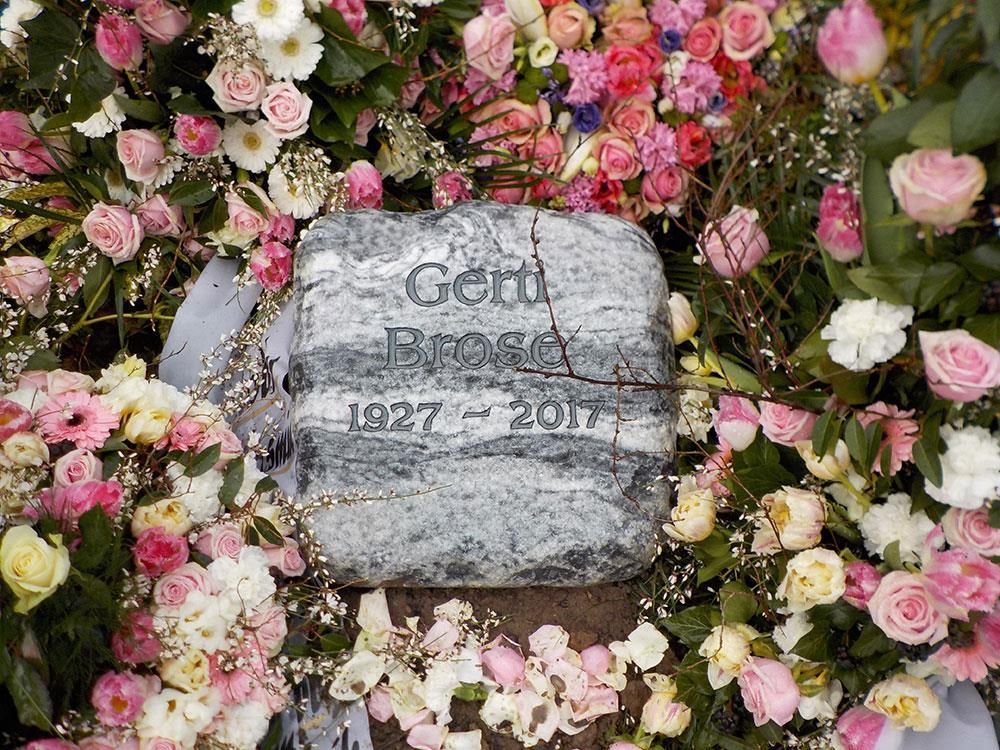 Ein Grabstein ist von rosa und weißen Blumen umgeben.