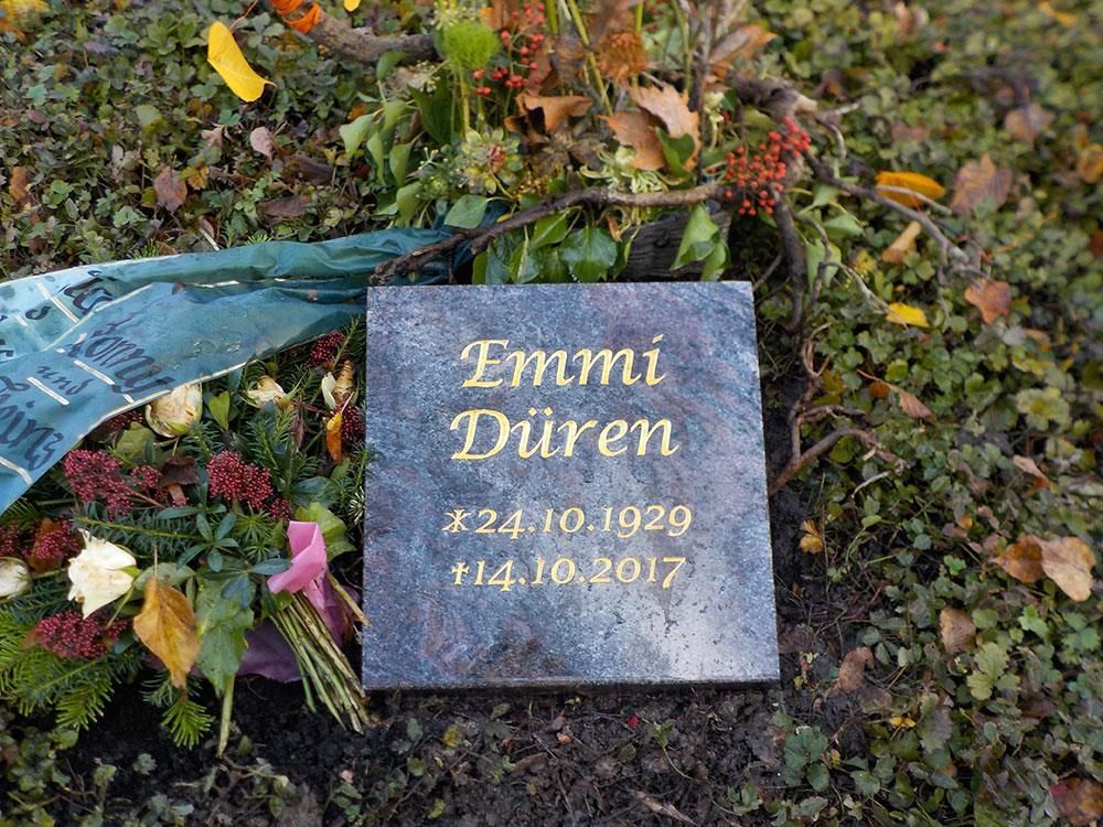 Ein Grabstein st von Blumen umgeben.