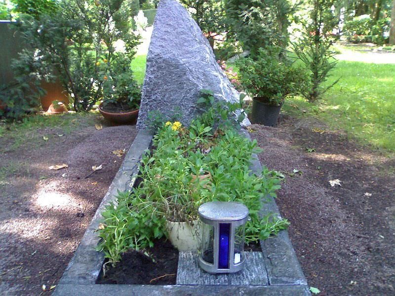 Ein Grab auf einem Friedhof mit einer blauen Laterne und Pflanzen
