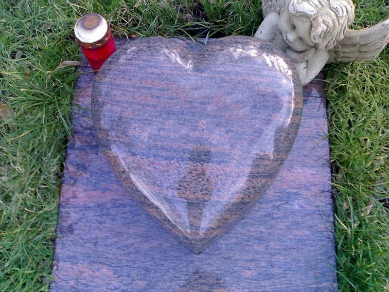 Ein herzförmiger Grabstein mit einer Kerze und einer Engelsstatue.