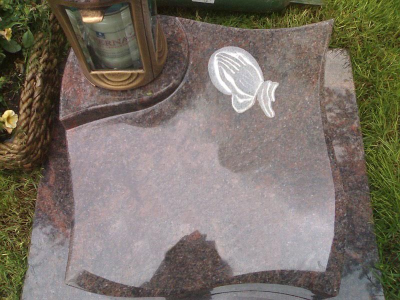 Ein Grabstein mit einer betenden Hand und einer Laterne darauf.