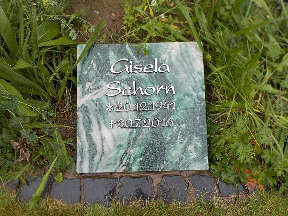 Eine Gedenktafel aus grünem Marmor liegt im Gras eines Friedhofs.