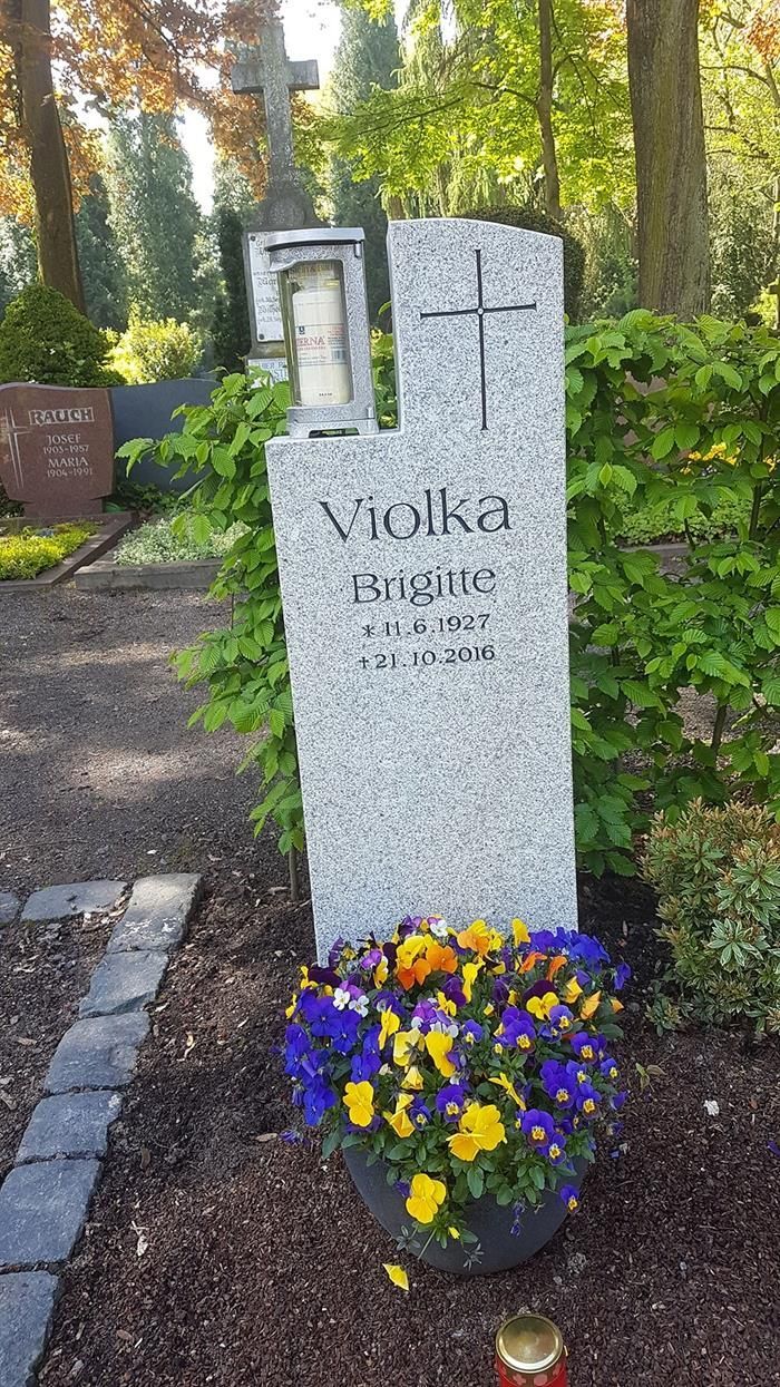 Ein Grabstein mit einem Kreuz und Blumen auf einem Friedhof.