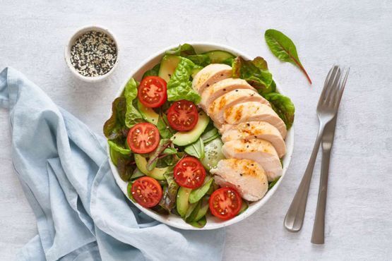 Un tazón de ensalada con pollo, tomates, pepinos y lechuga.