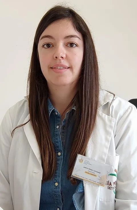 Una mujer lleva una bata de laboratorio blanca y una etiqueta con su nombre.