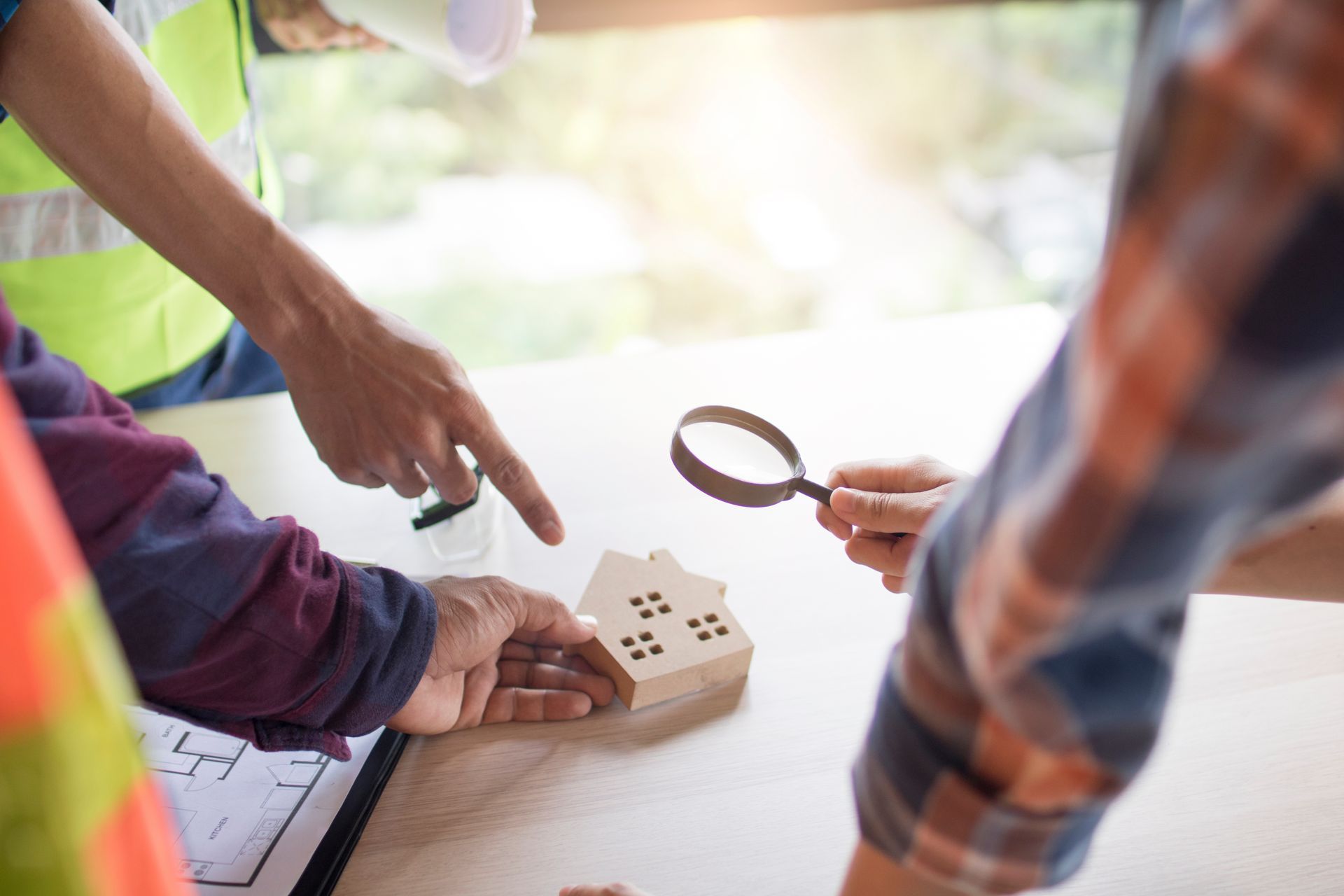 Des professionnels examinent une petite maquette de maison en bois posée sur une table, à l'aide d'une loupe et de plans.