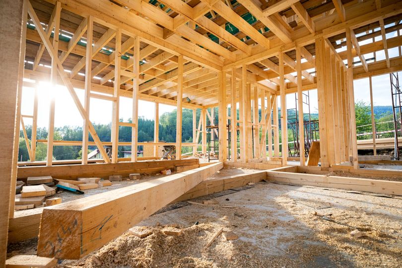 Charpente en bois d'une maison en construction, laissant entrer la lumière du soleil à travers la structure ouverte.
