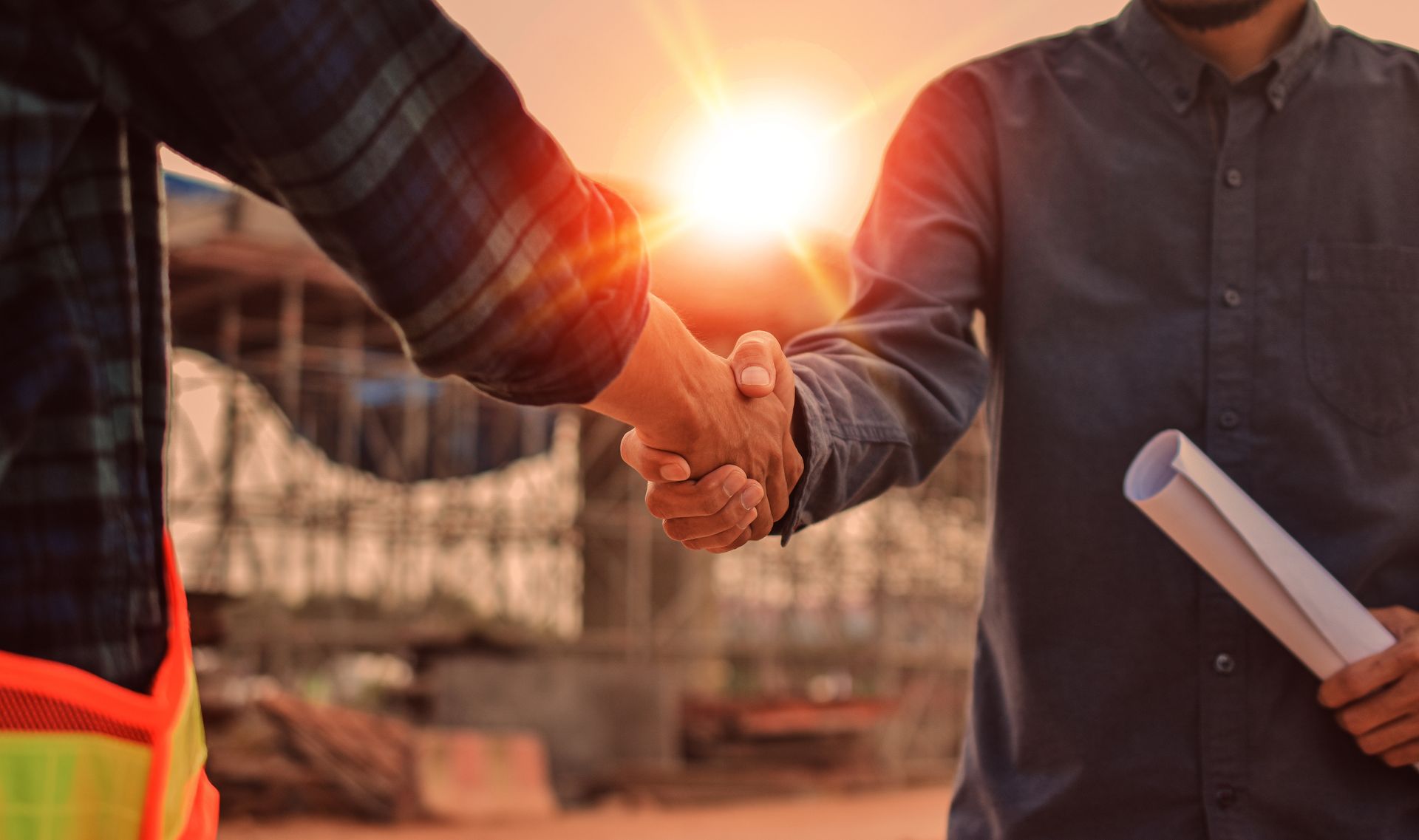 Deux personnes se serrent la main sur un chantier au coucher du soleil.