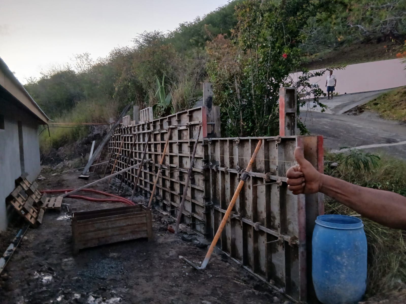 Une personne lève le pouce à côté de panneaux de coffrage modulaires en béton en cours d'installation sur un chantier de construction résidentielle.