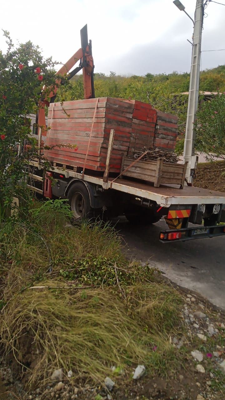 Un camion plateau stationné en bord de route, chargé d'une grande pile de pavés en pierre rouge et d'une caisse en bois.