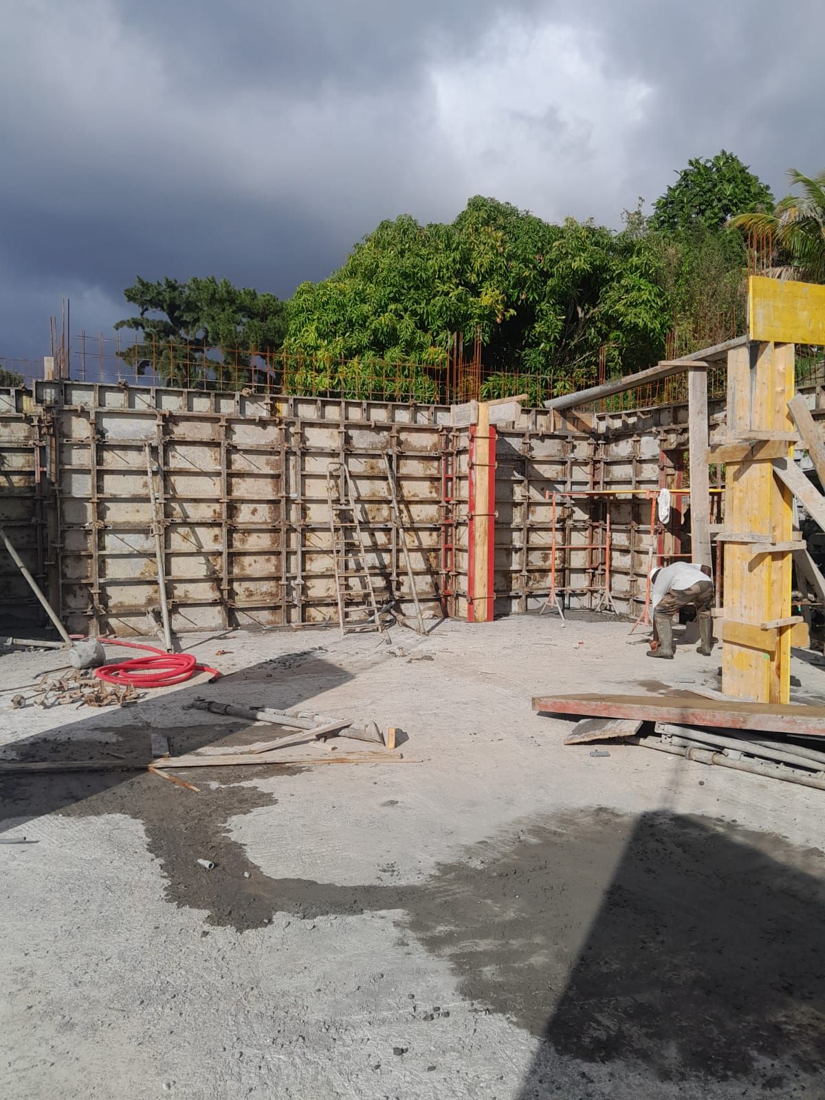 Un mur de soutènement en béton soutient un talus herbeux surmonté de maisons, visible depuis un parking pavé.