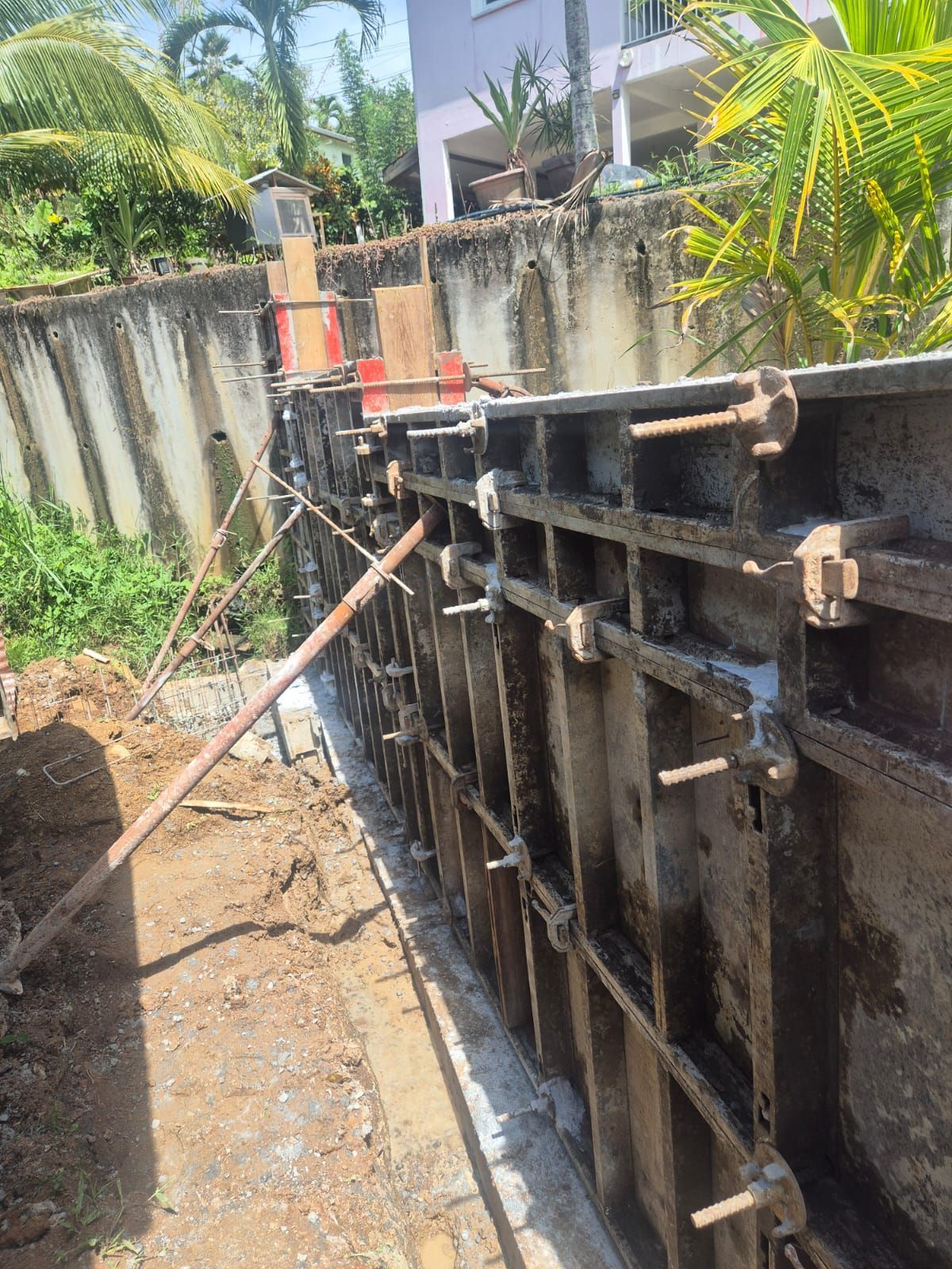 Une structure de coffrage métallique en béton pour un mur en construction à l'extérieur, renforcée par des planches et des supports en bois.