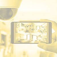 Une main tenant un smartphone relié à un système de surveillance vidéo