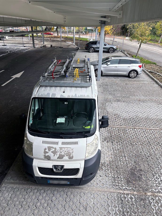 Camionnette blanche de chez Acelec sur un parking protégé.