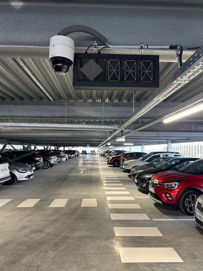 Parking avec voitures garées en rangées. Une caméra et un écran qui affichent les places disponibles
