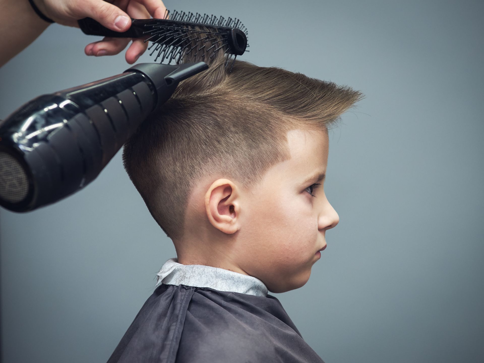 Ein kleiner Junge lässt sich von einem Friseur die Haare föhnen.