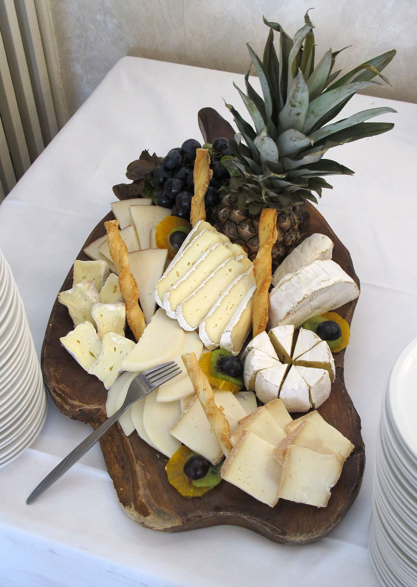 A wooden cutting board filled with cheese and fruit with a pineapple on top.