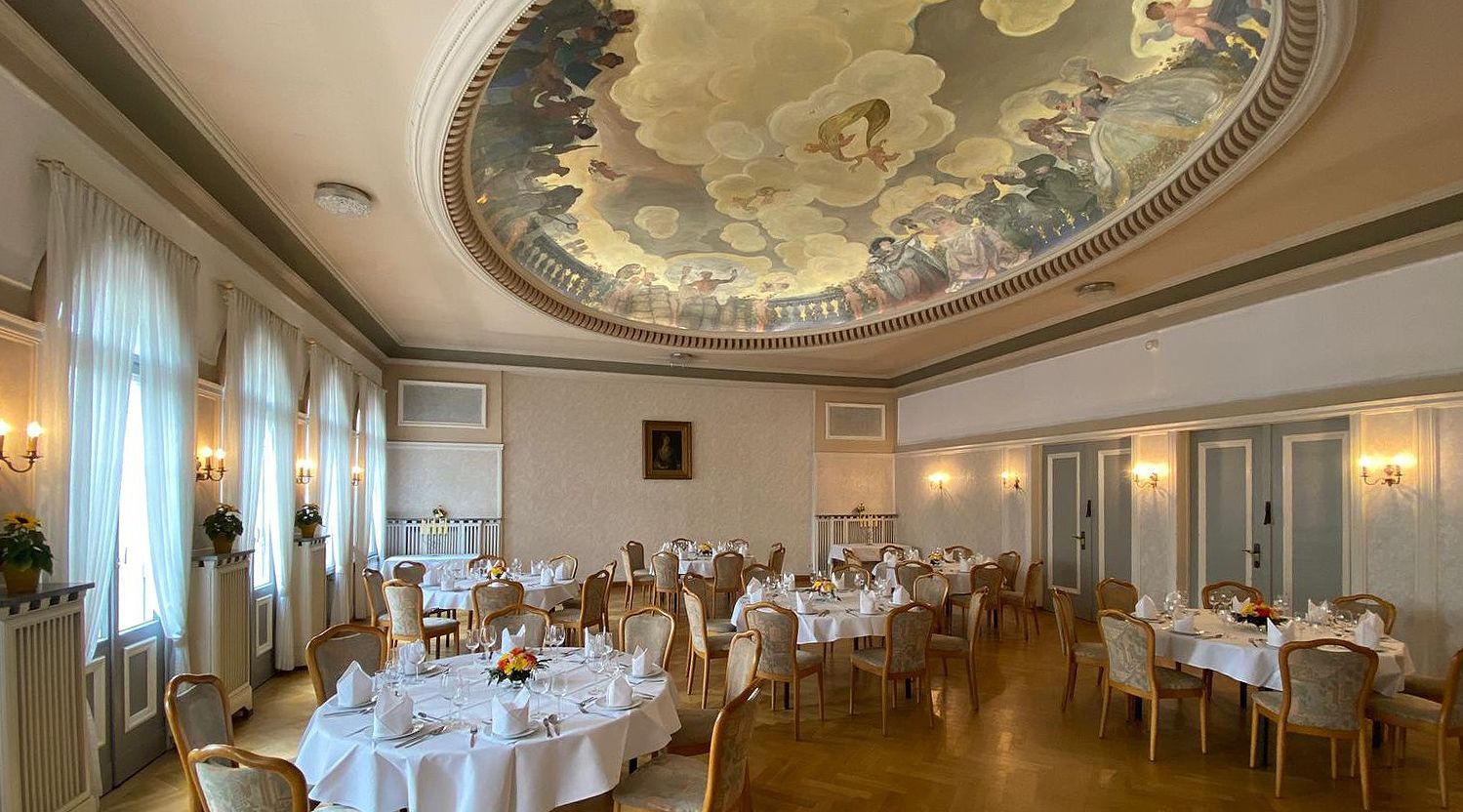 A large dining room with tables and chairs and a painting on the ceiling.