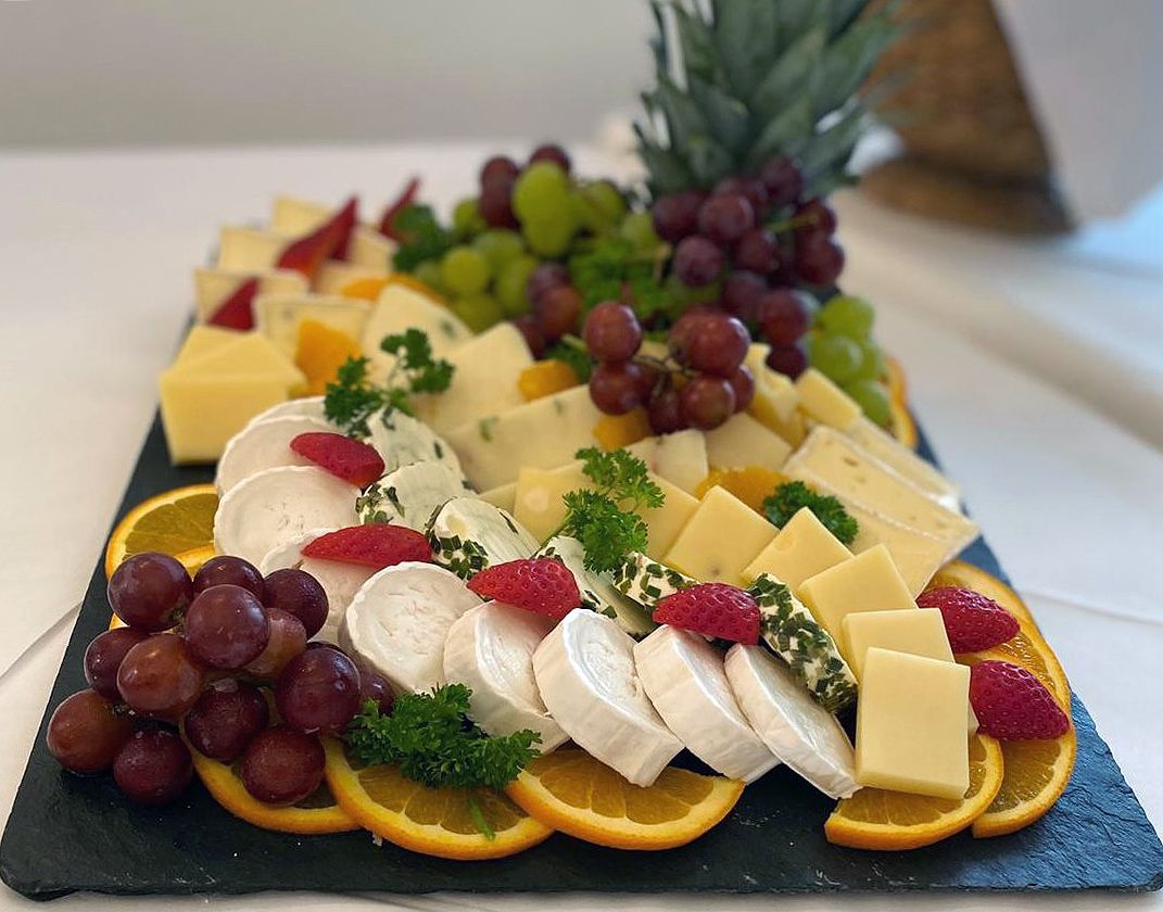 Ein Tablett mit Käse, Trauben, Orangen und Himbeeren auf einem Tisch.