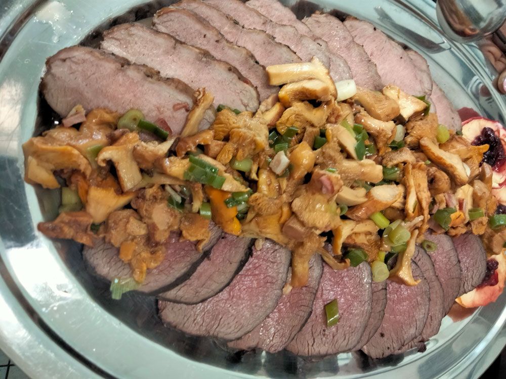 Gegrilltes Wildsteak mit Rosmarin, Pfefferkörnern, Knoblauch und Meersalz auf einem Holzteller.