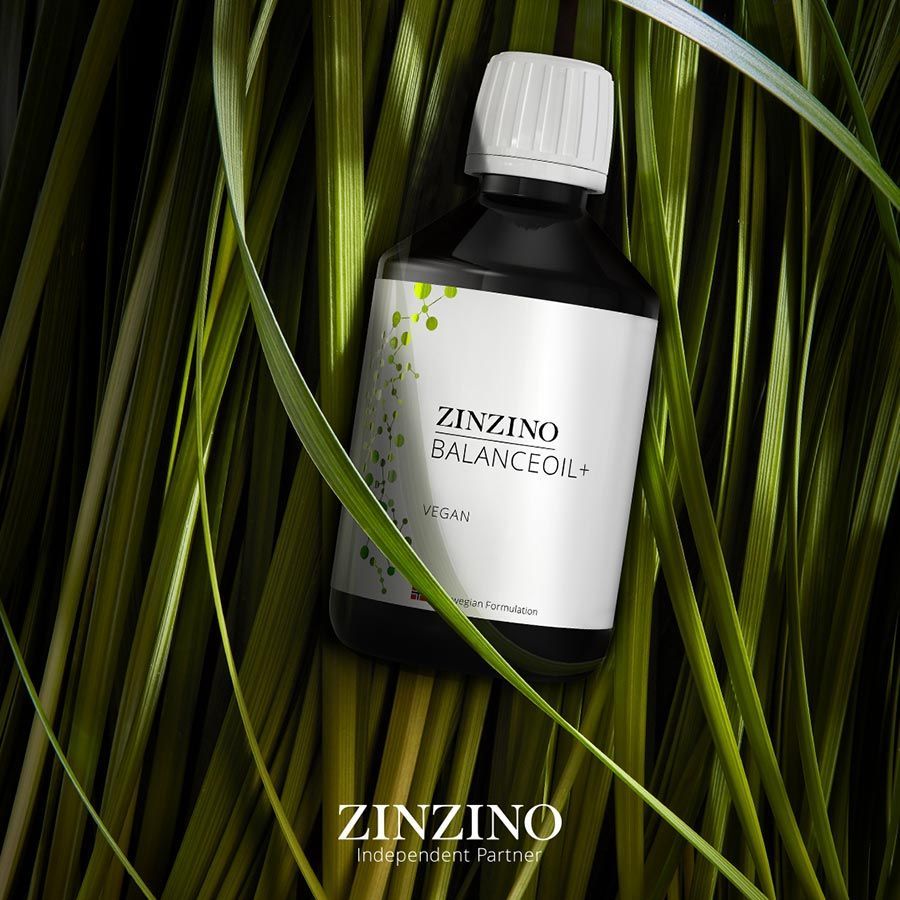 Botella oscura de Zinzino BalanceOil con tapón blanco sobre hojas verdes, etiqueta visible