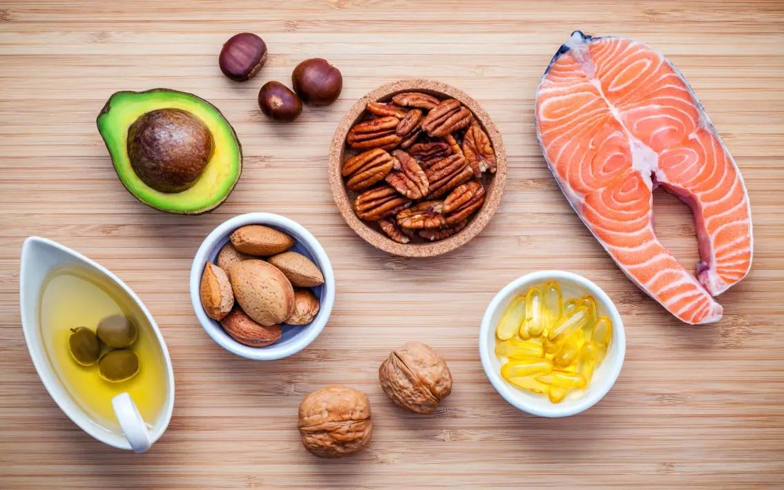 Una mesa de madera cubierta con cuencos de nueces, pescado, aguacate y aceite.