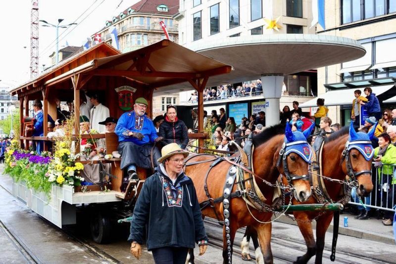 Eine von Pferden gezogene Kutsche in einer Parade, Menschen in traditioneller Kleidung, geschmückt mit Blumen.