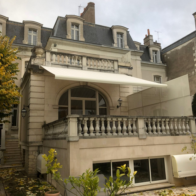 Immeuble ancien avec balcon, fenêtre cintrée, store à banne déployée.