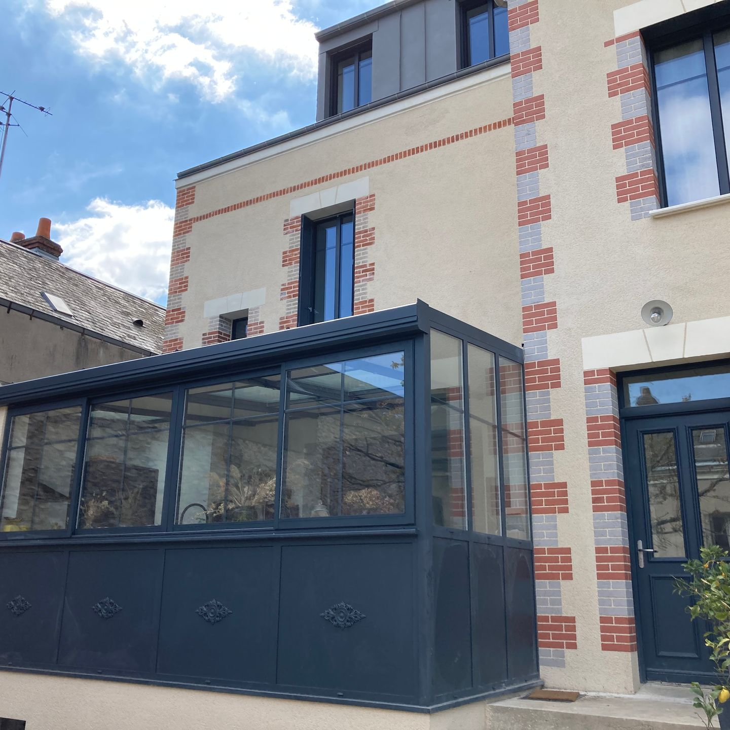 Maison beige à deux étages avec une véranda bleu foncé. Murs et façades en briques.