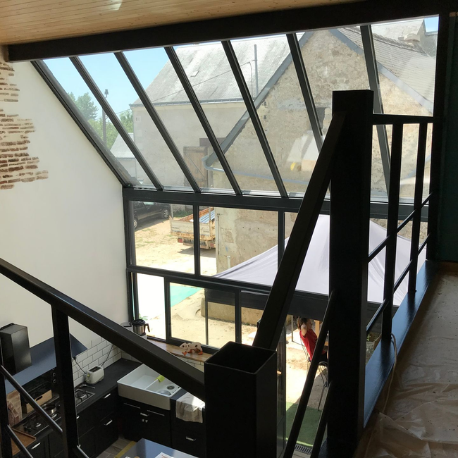 Vue intérieure d'un loft moderne avec une grande baie vitrée donnant sur d'autres bâtiments en pierre.