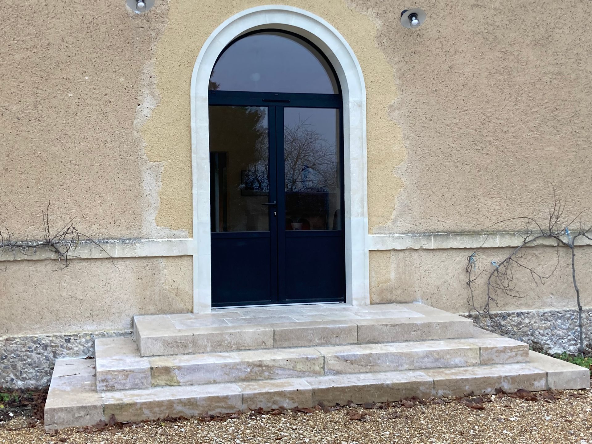 Une porte d'entrée cintrée bleu foncé avec imposte latérale, des marches en pierre.