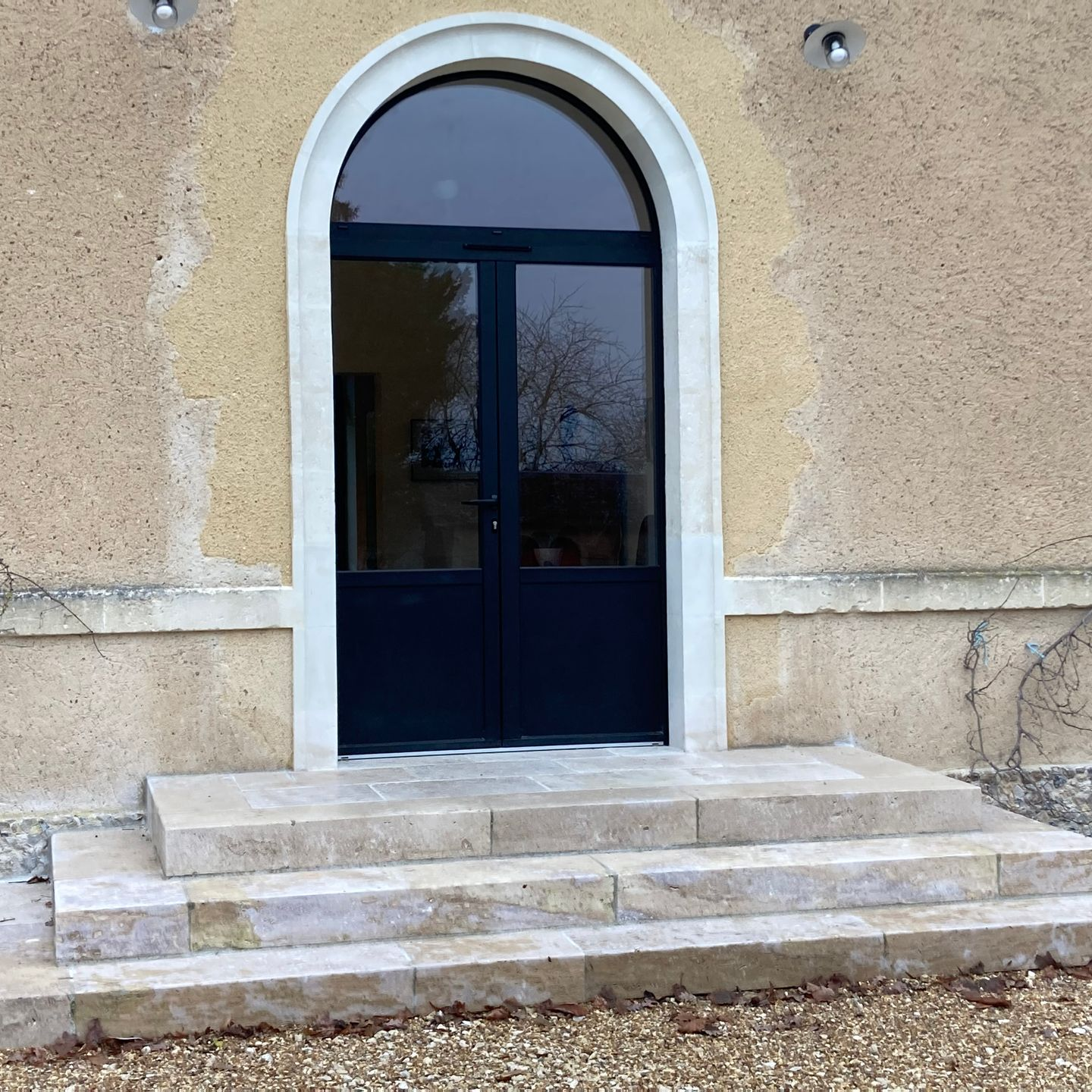Une porte cintrée bleu foncé avec imposte latérale, des marches en pierre.