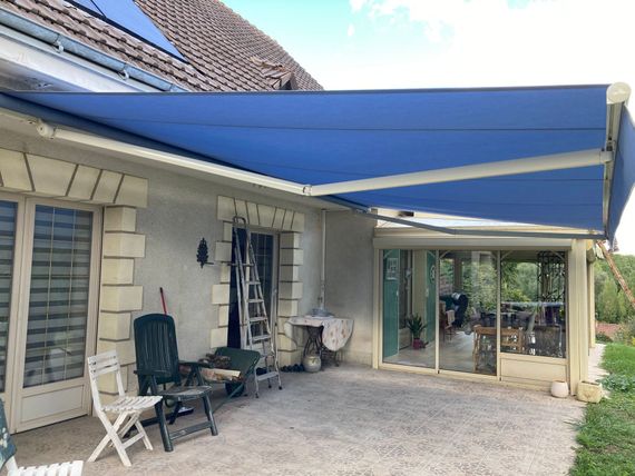 Un store à banne bleue ouvert au-dessus d'une terrasse.