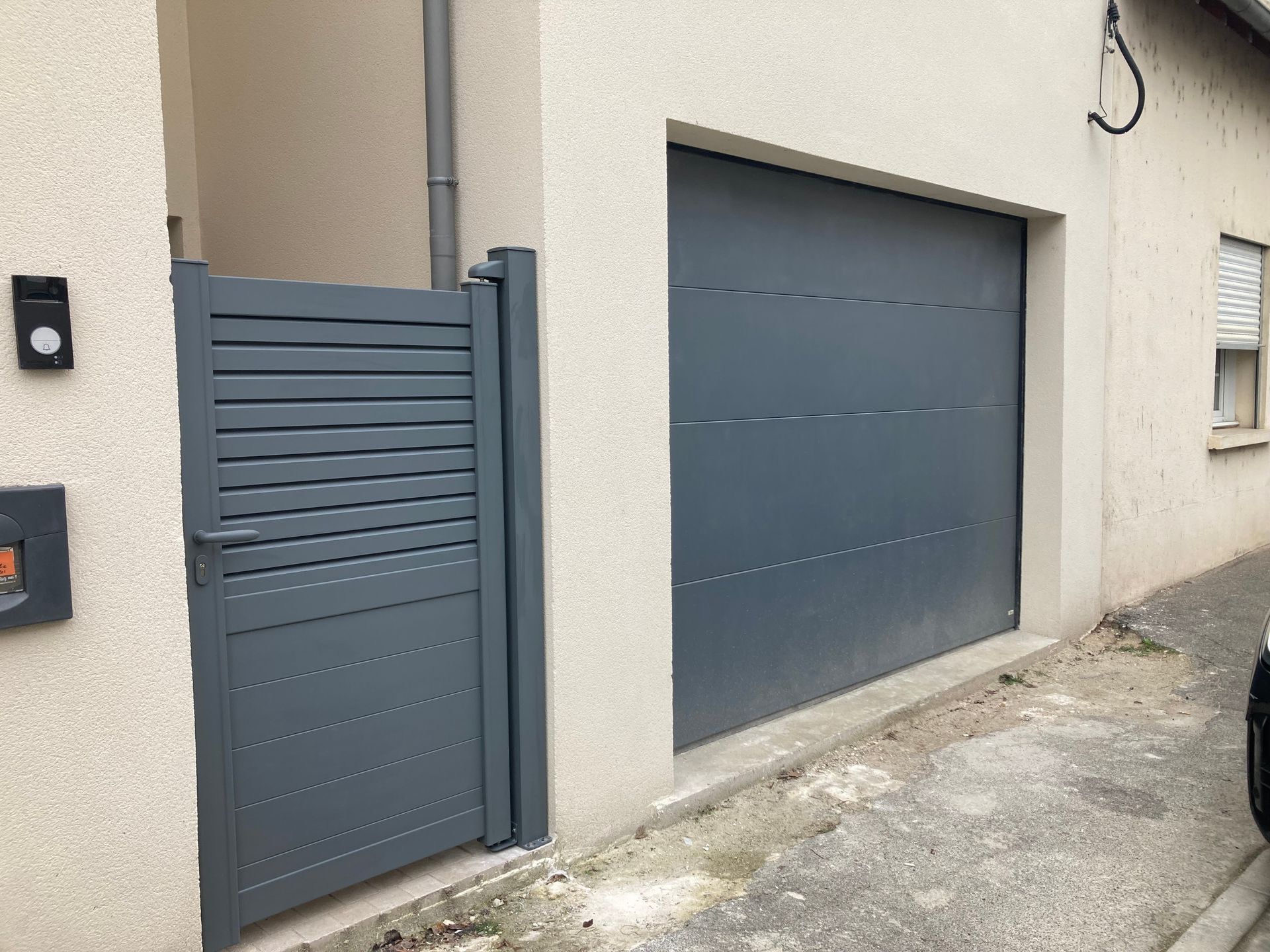 Portail et porte de garage gris sur la façade d'un bâtiment aux couleurs claires.