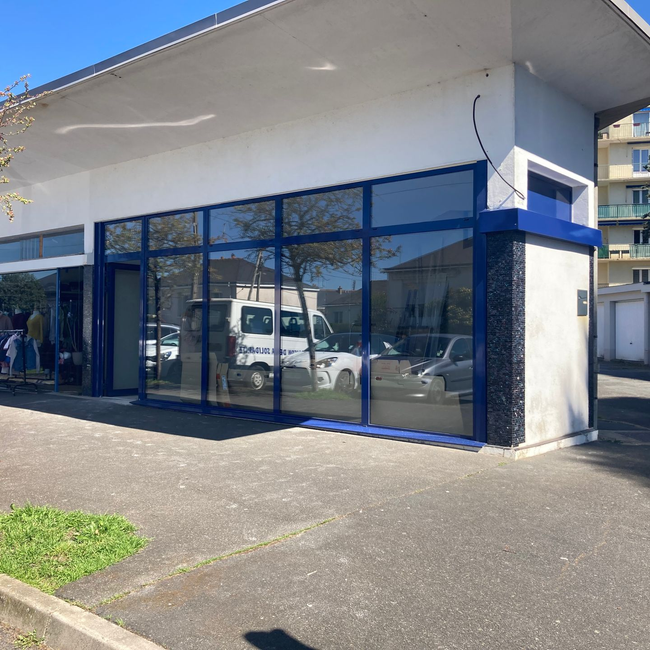 Extérieur d'un bâtiment commercial avec de grandes fenêtres reflétant les véhicules.