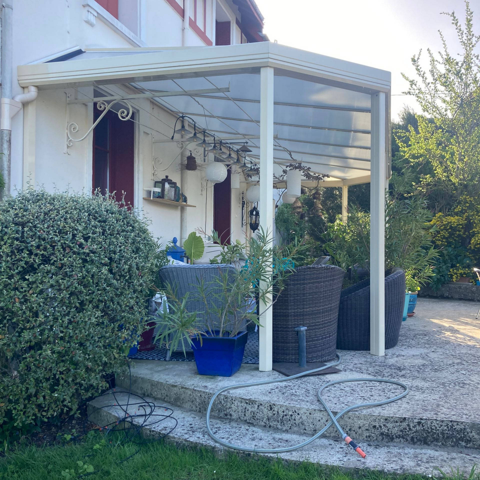 Une terrasse couverte d'un abri en aluminium blanc avec des plantes en pot et des sièges.