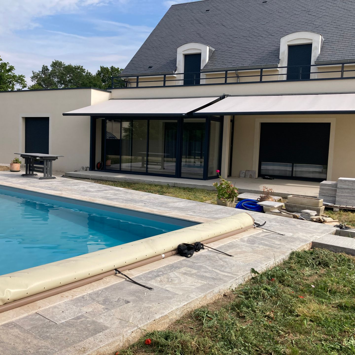 Vue depuis la piscine d'une maison avec piscine et double store à banne ouvert.