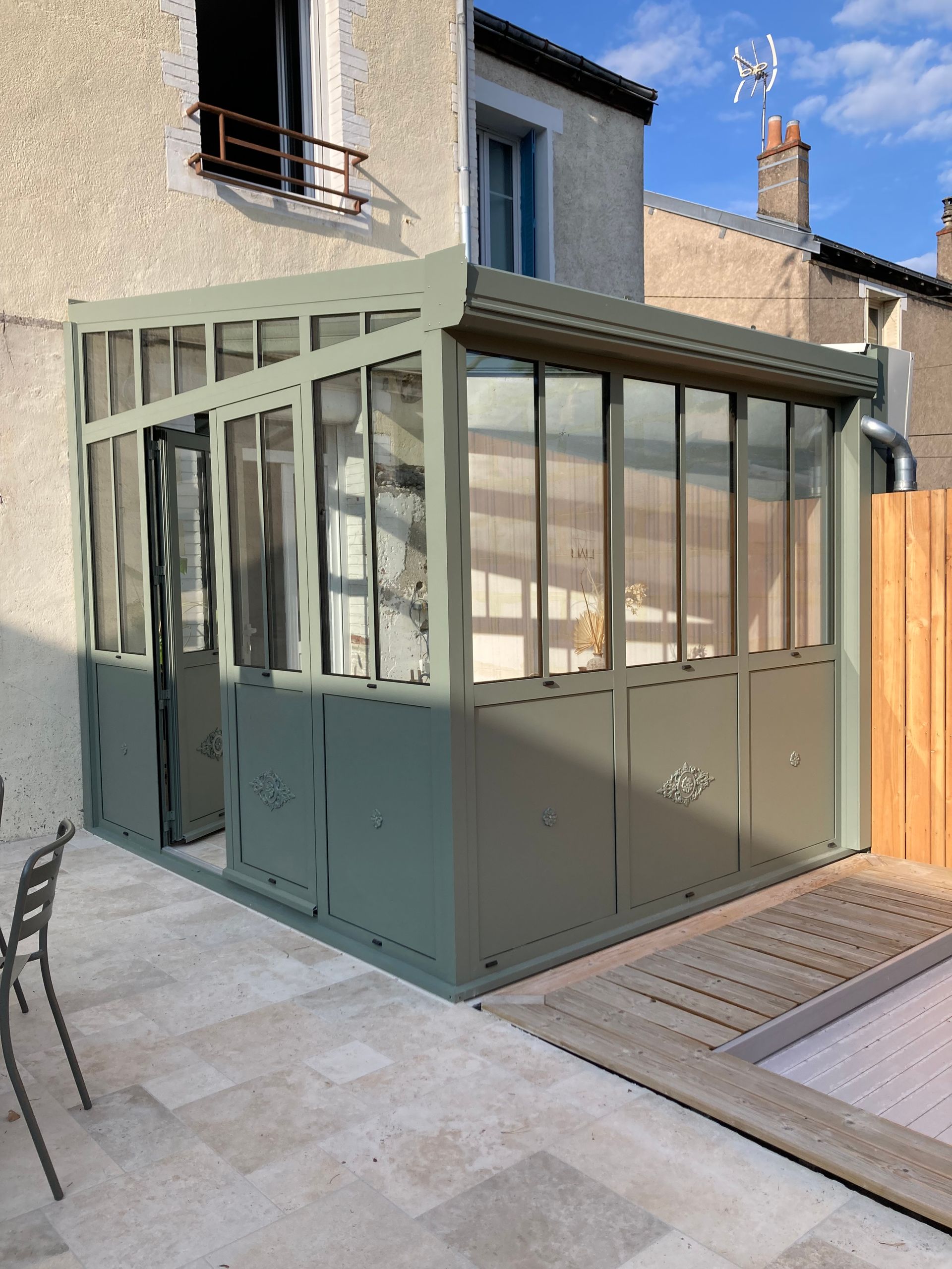 Véranda neuve en aluminium noir contre une petite maison de ville au fond d'une cour.